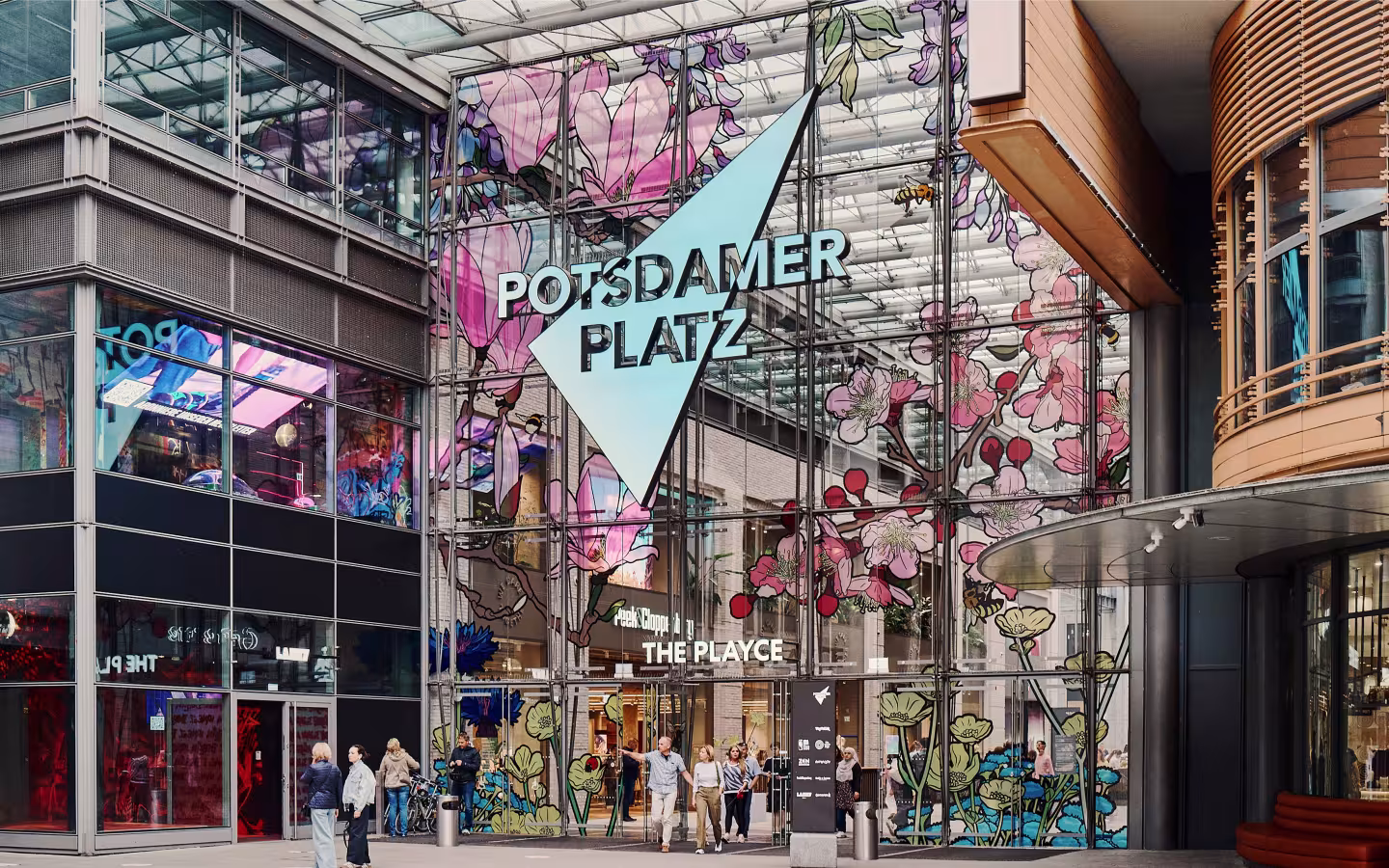 Street-level view of Potsdamer Platz, a BGRE mixed-use office and retail destination in Berlin, featuring The Playce retail centre entrance and visitors in the public space.