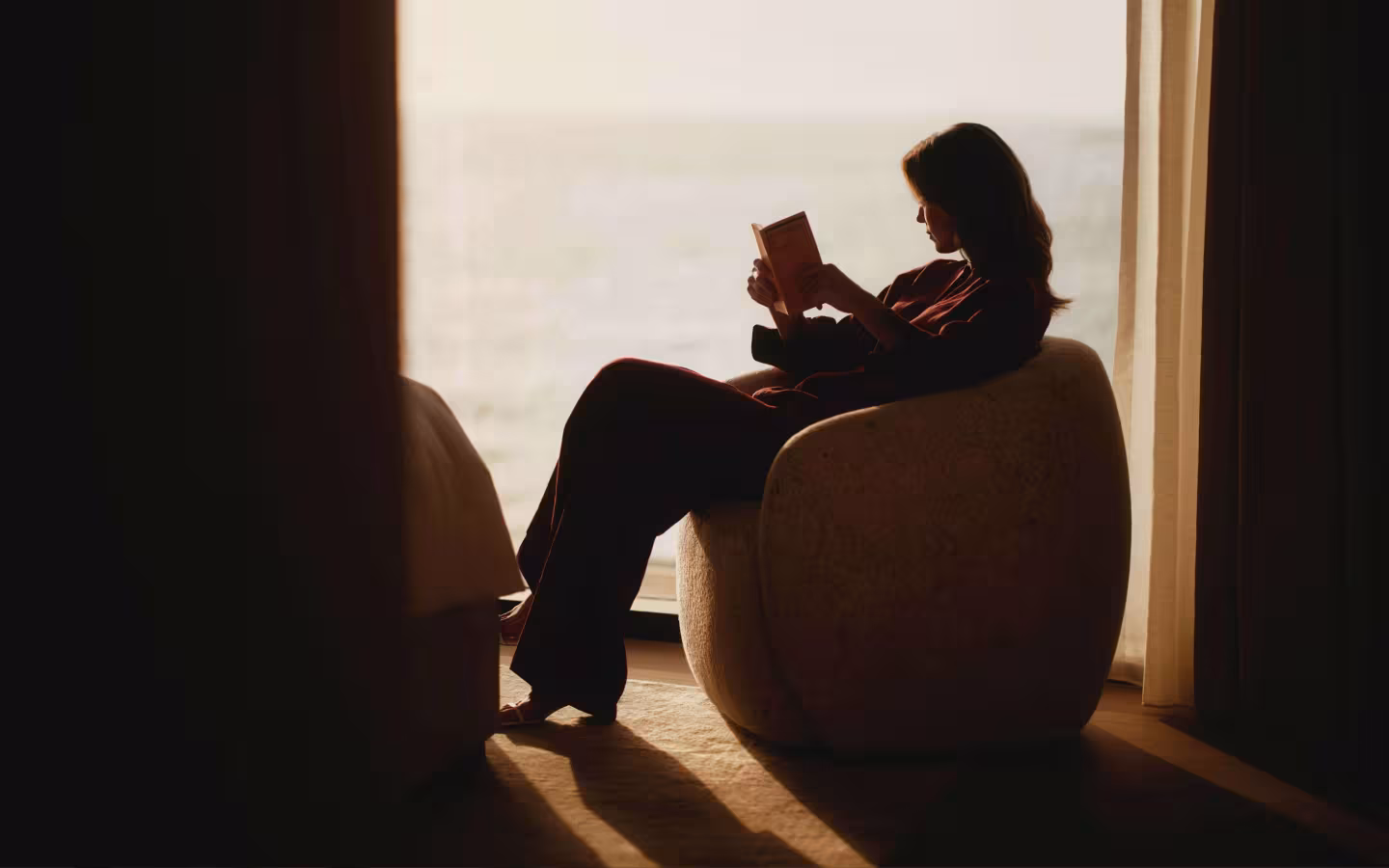 Interior view of Solaya, a contemporary BGRE residential community in Jumeirah Dubai, featuring a resident reading beside a floor-to-ceiling window with contemporary furnishings and waterfront views.