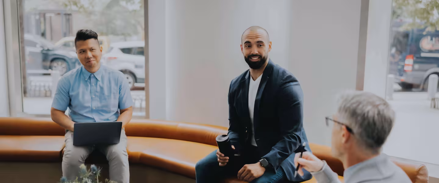Three colleagues talk casually in a bright lobby
