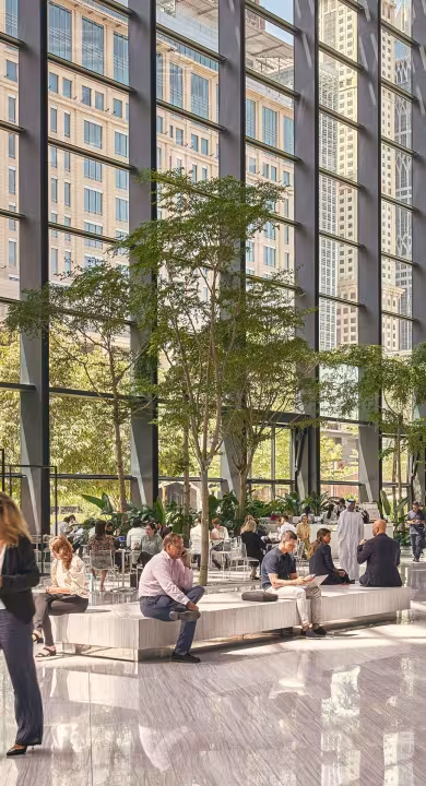 Interior view of a BGRE office property, showing a light-filled glass atrium, indoor greenery, and occupants gathering, working and moving through the space.